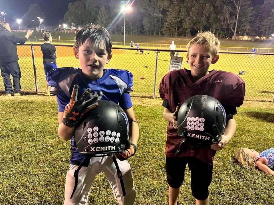 Two young boys are holding football helmets on a field.