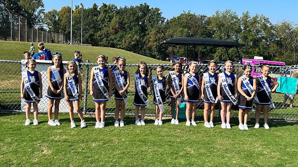 A group of cheerleaders are standing in a row on a field.