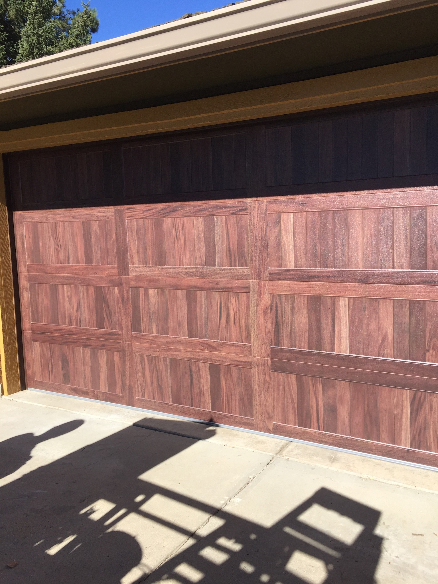 A wooden garage door with a shadow on the sidewalk.