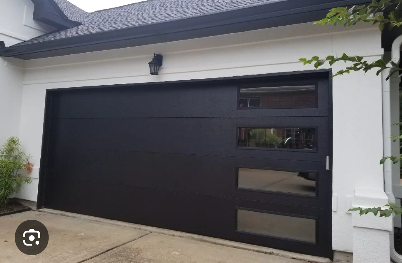 A black garage door is on a white house.
