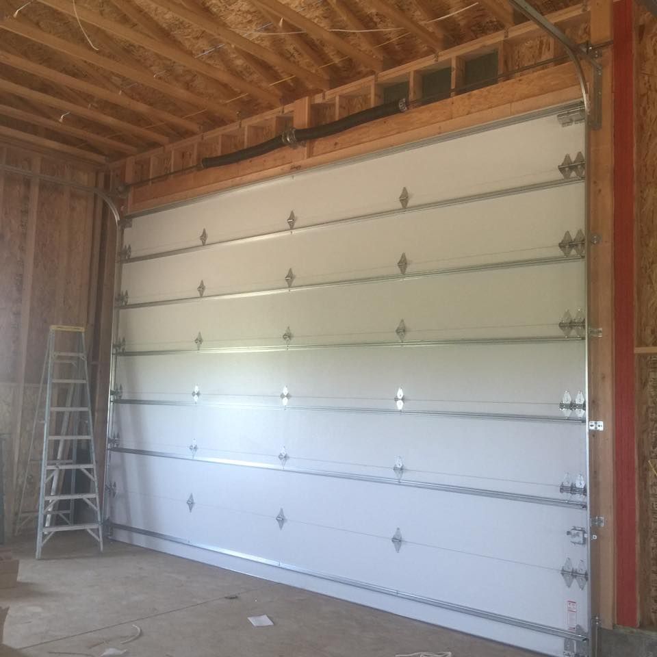 A large white garage door is open in a room with a ladder.