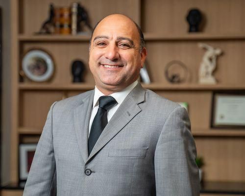 A man in a suit and tie is smiling in front of a bookshelf.