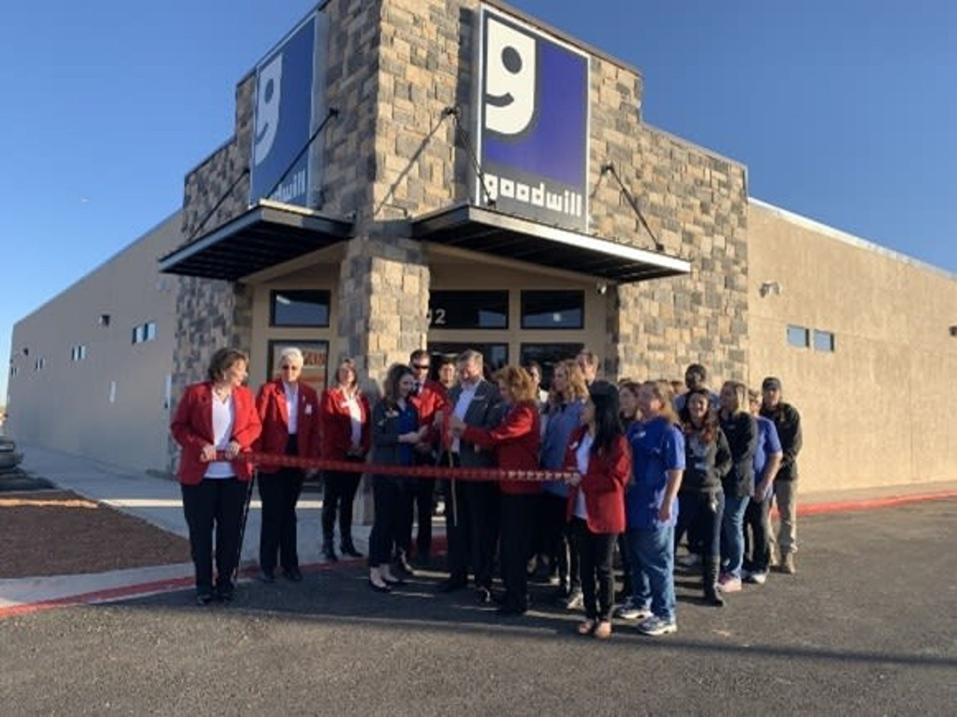 Goodwill store ribbon-cutting: group of people, red ribbon, blue logo.