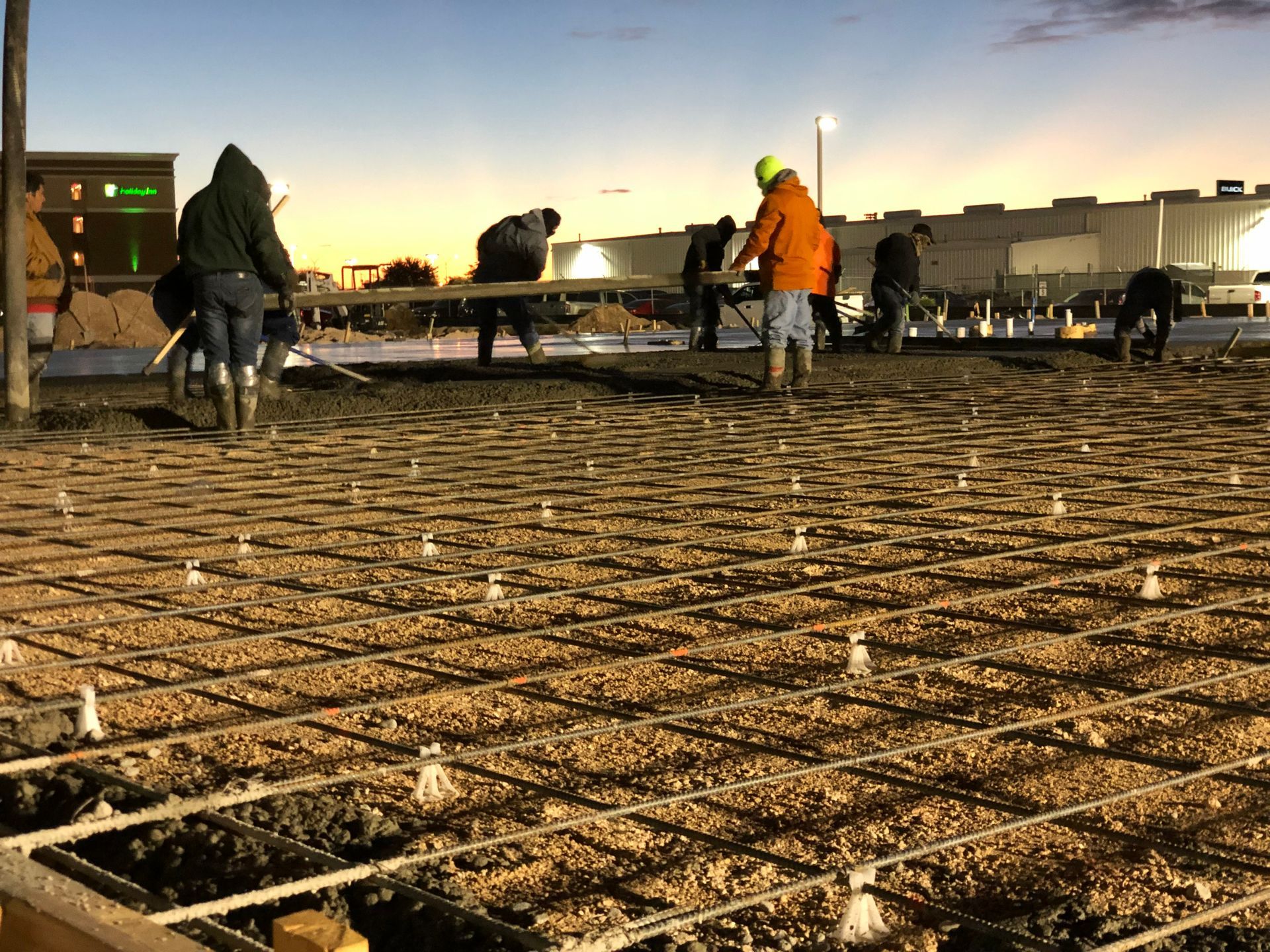 Construction workers pouring concrete on rebar, dusk setting.