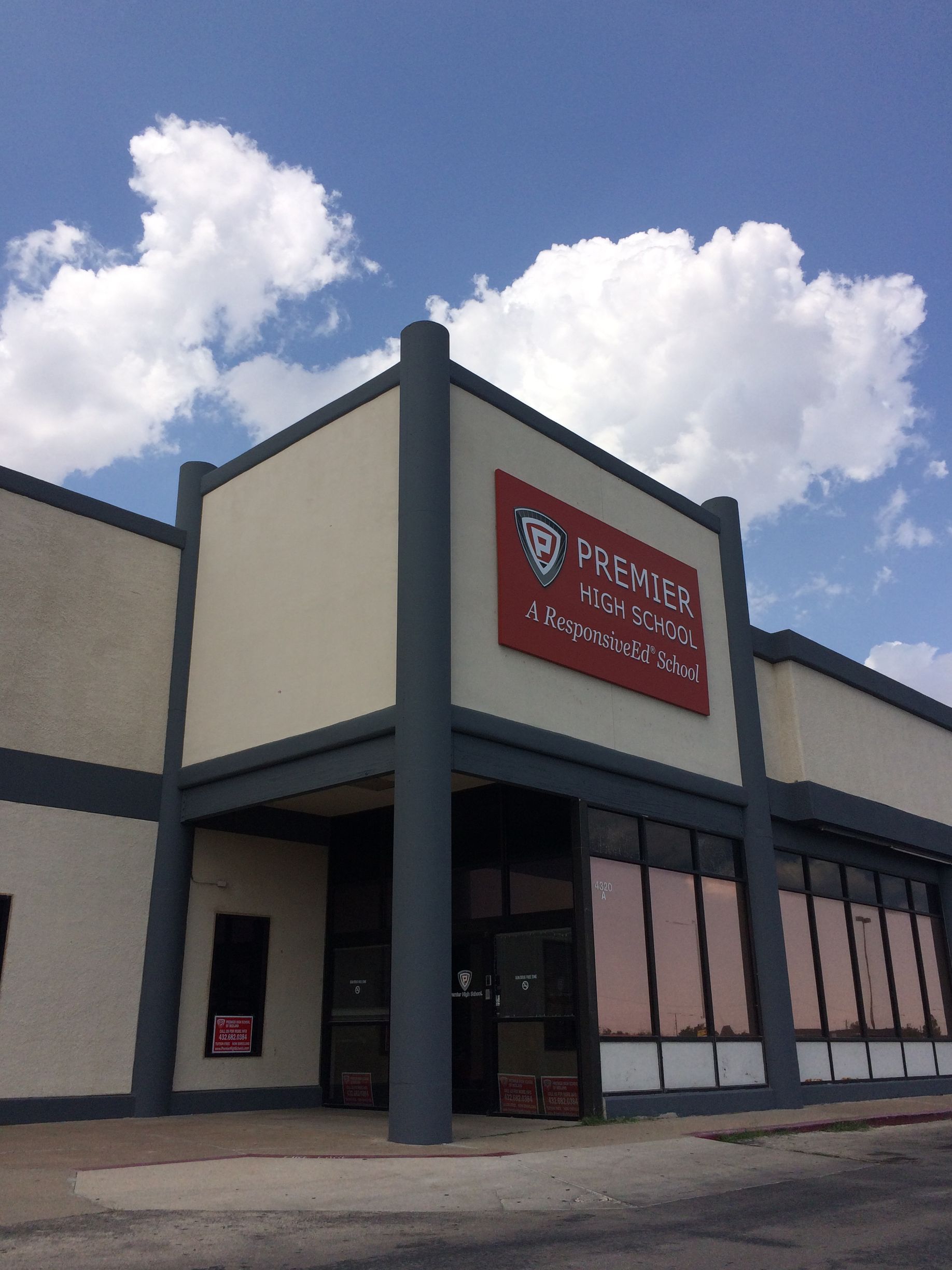 Modern building with glass facade, vertical gray stripes, and surrounding green trees under a blue sky.