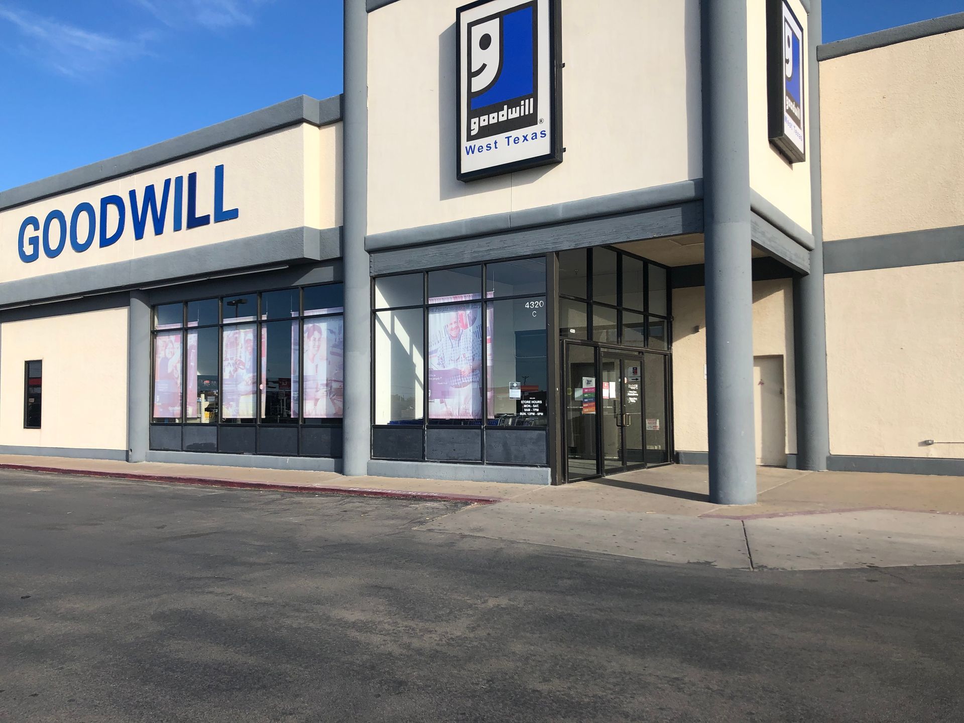 Exterior of a Goodwill store; blue and white building, glass windows, sign with logo.