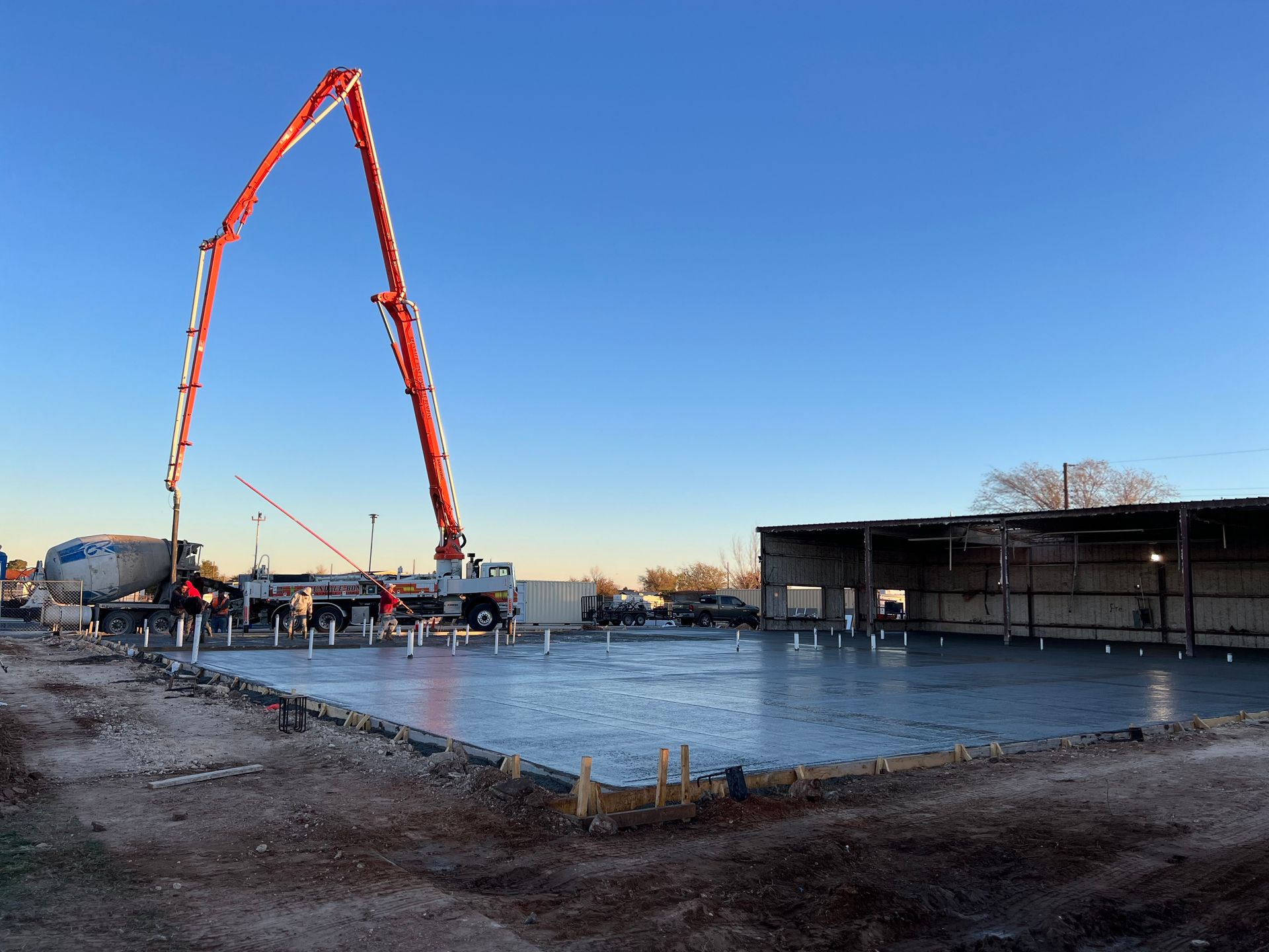 A concrete pour on a construction site. A pump truck extends its boom over a fresh concrete slab. Clear, blue sky.