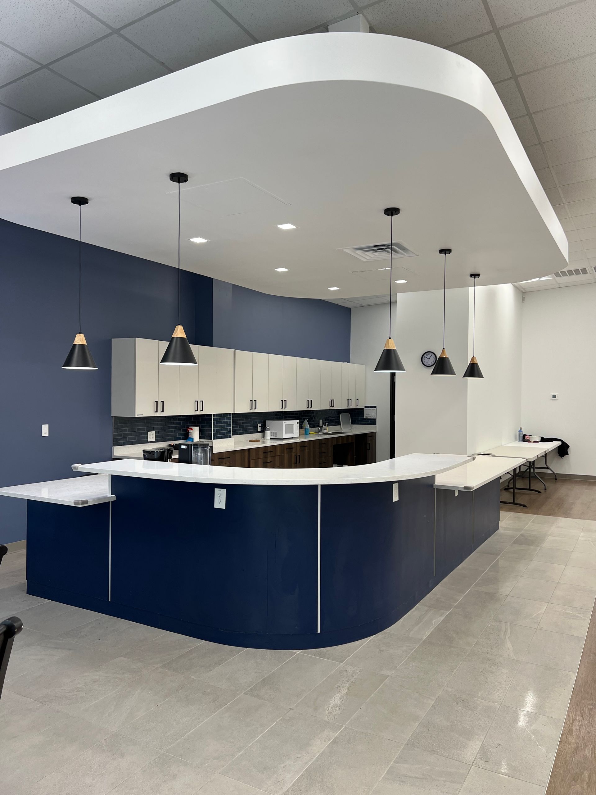Modern office space with a curved, blue-paneled counter, overhead cabinets, and pendant lights.