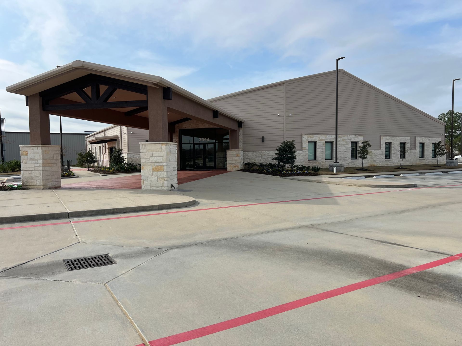 Building with covered entrance, beige walls, and parking area under a cloudy sky.