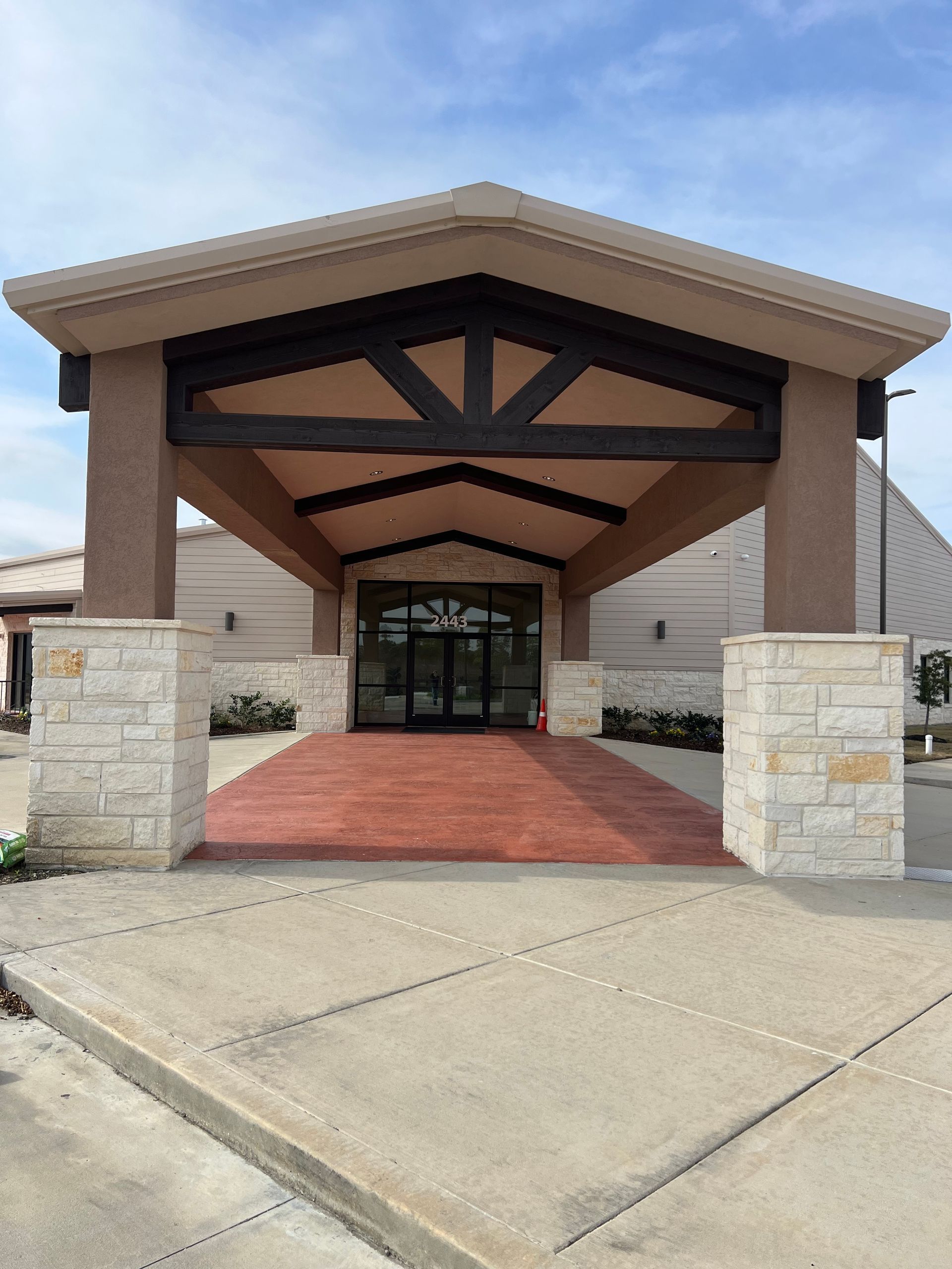 Building entrance with red brick walkway and stone columns under a tan awning.