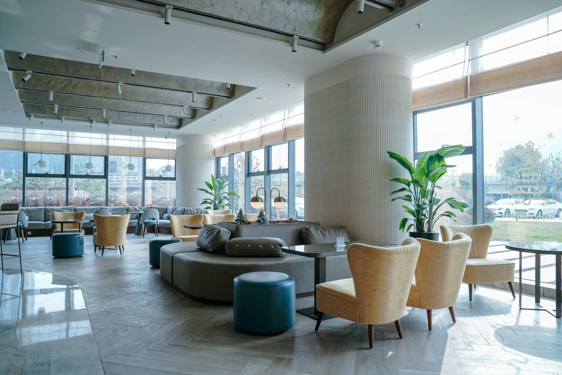 Bright modern hotel lobby with seating areas, large windows, and a column.