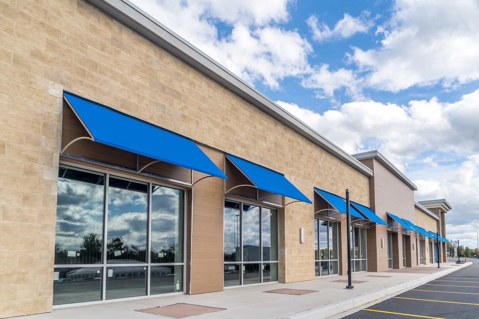 Commercial building with large windows, blue awnings, and a brick facade under a partly cloudy sky.