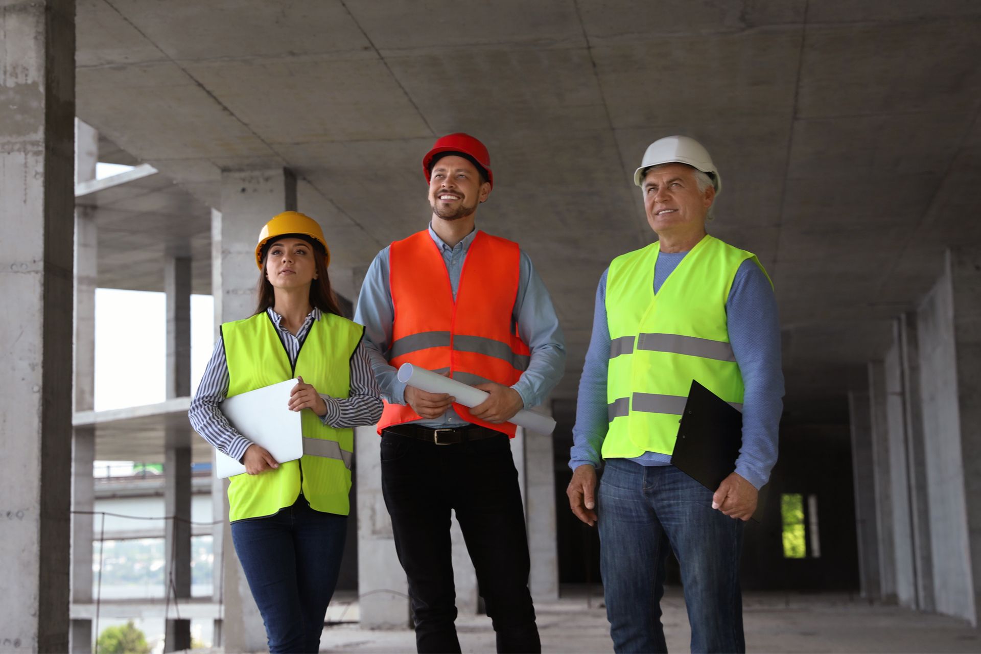 Three construction workers in hard hats and vests inside a building under construction.