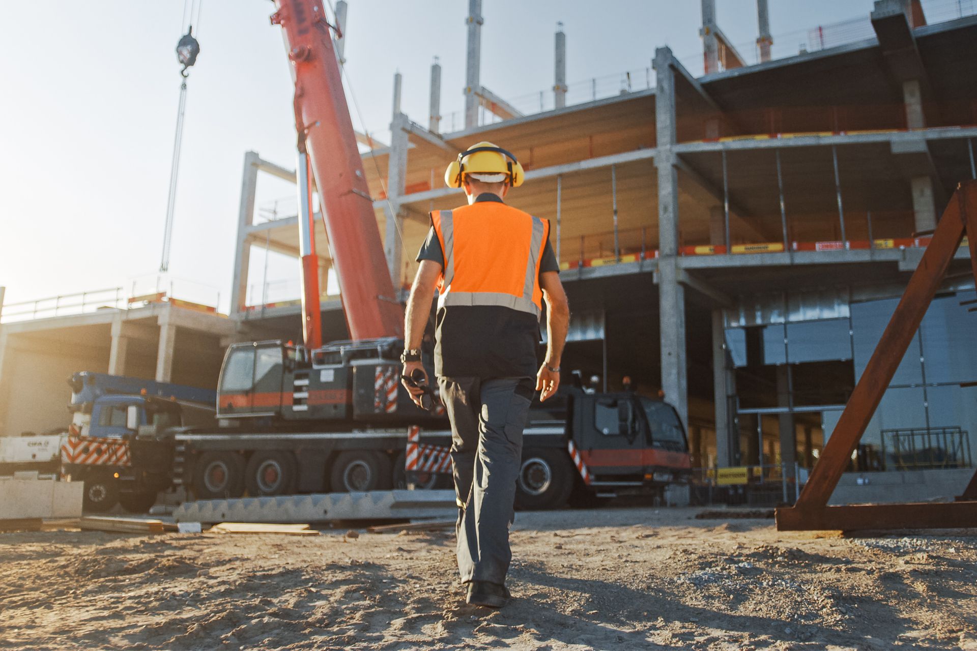 Construction worker walks toward a crane at a building site, wearing safety gear.