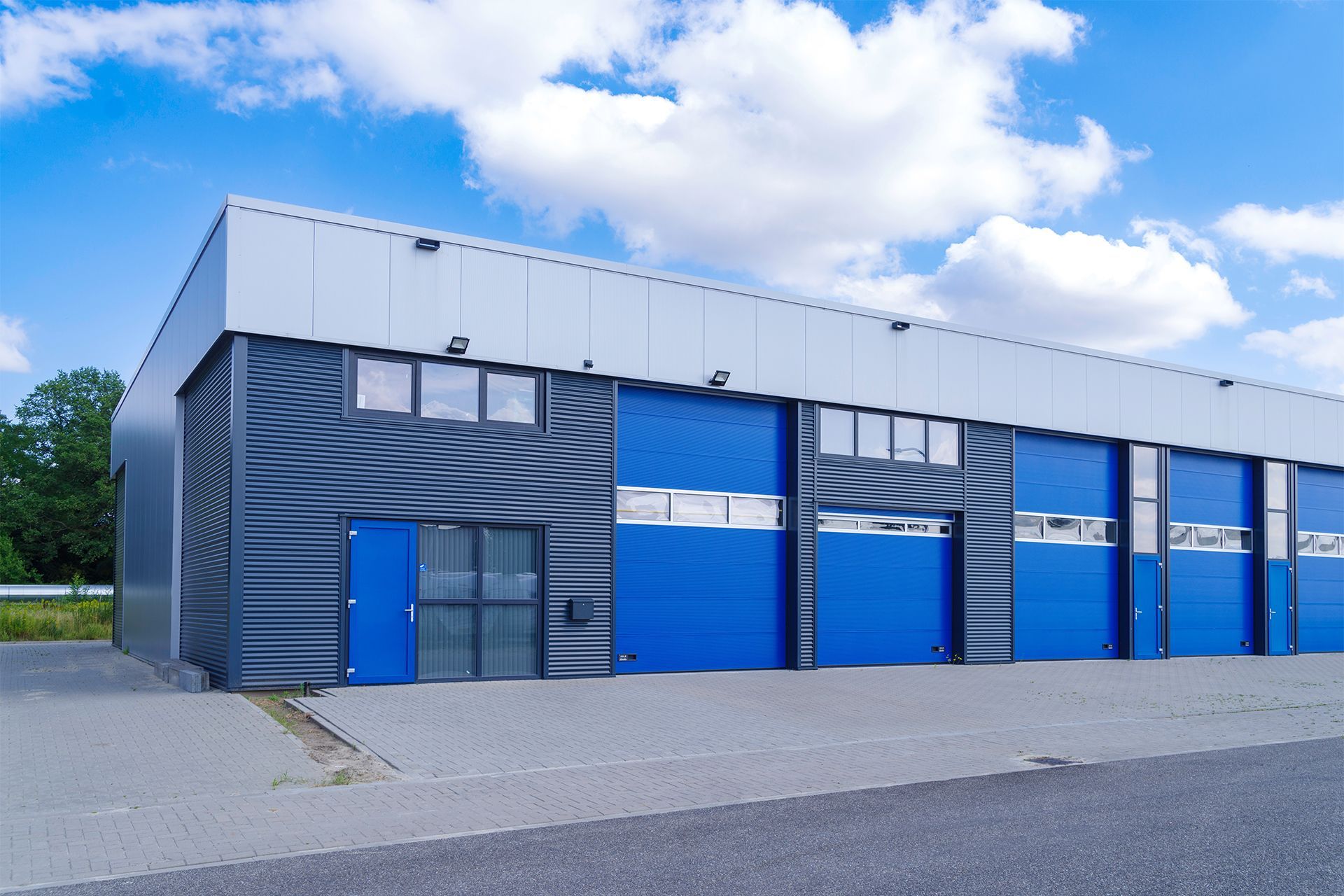 Blue and gray industrial building with large garage doors and blue accents under a partly cloudy sky.