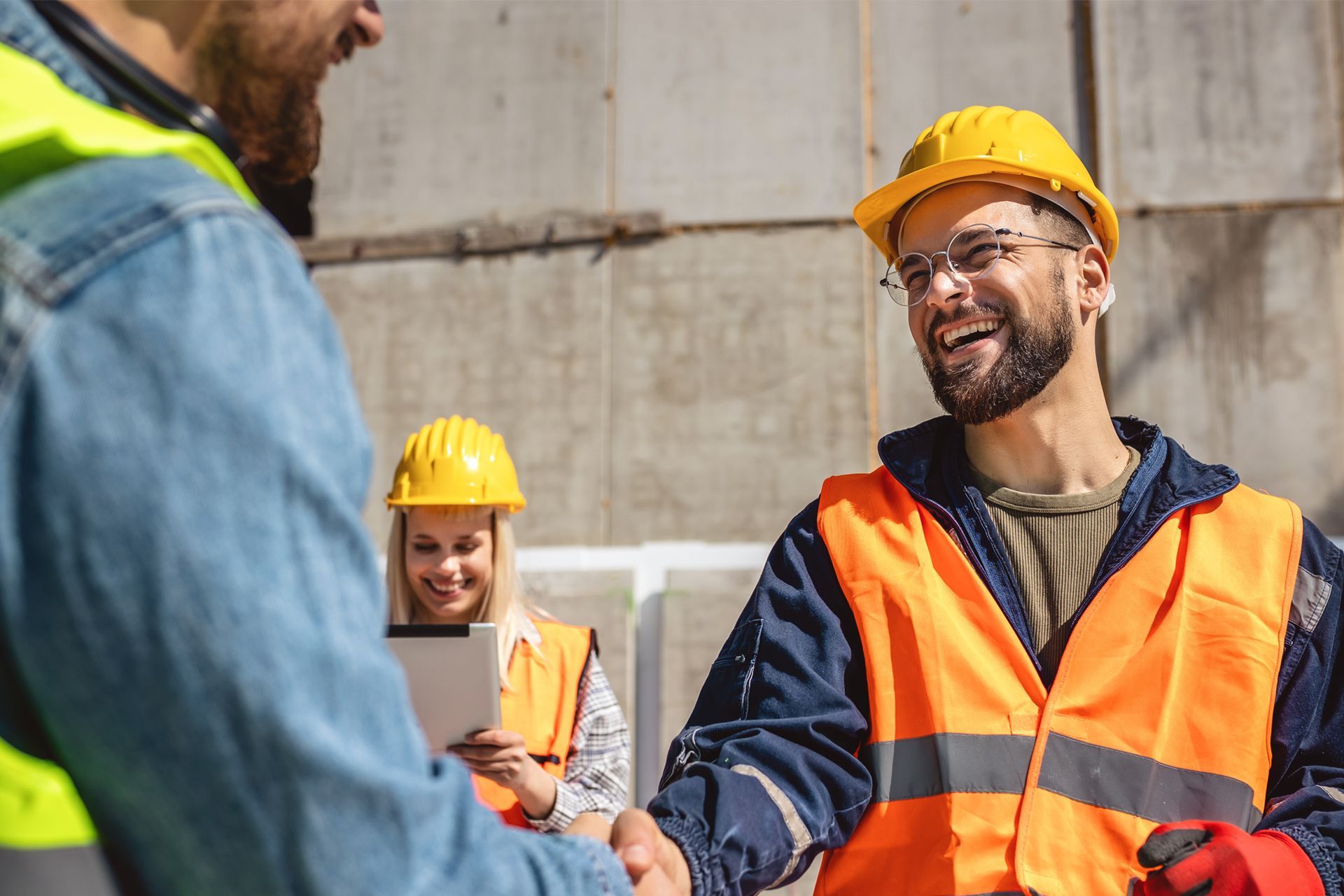 Construction workers shaking hands, smiling, wearing hard hats and safety vests.