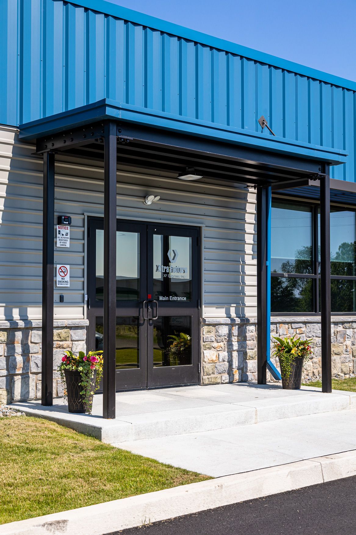 The entrance to the Xtra Factors East Earl, PA building with a blue roof and black doors.