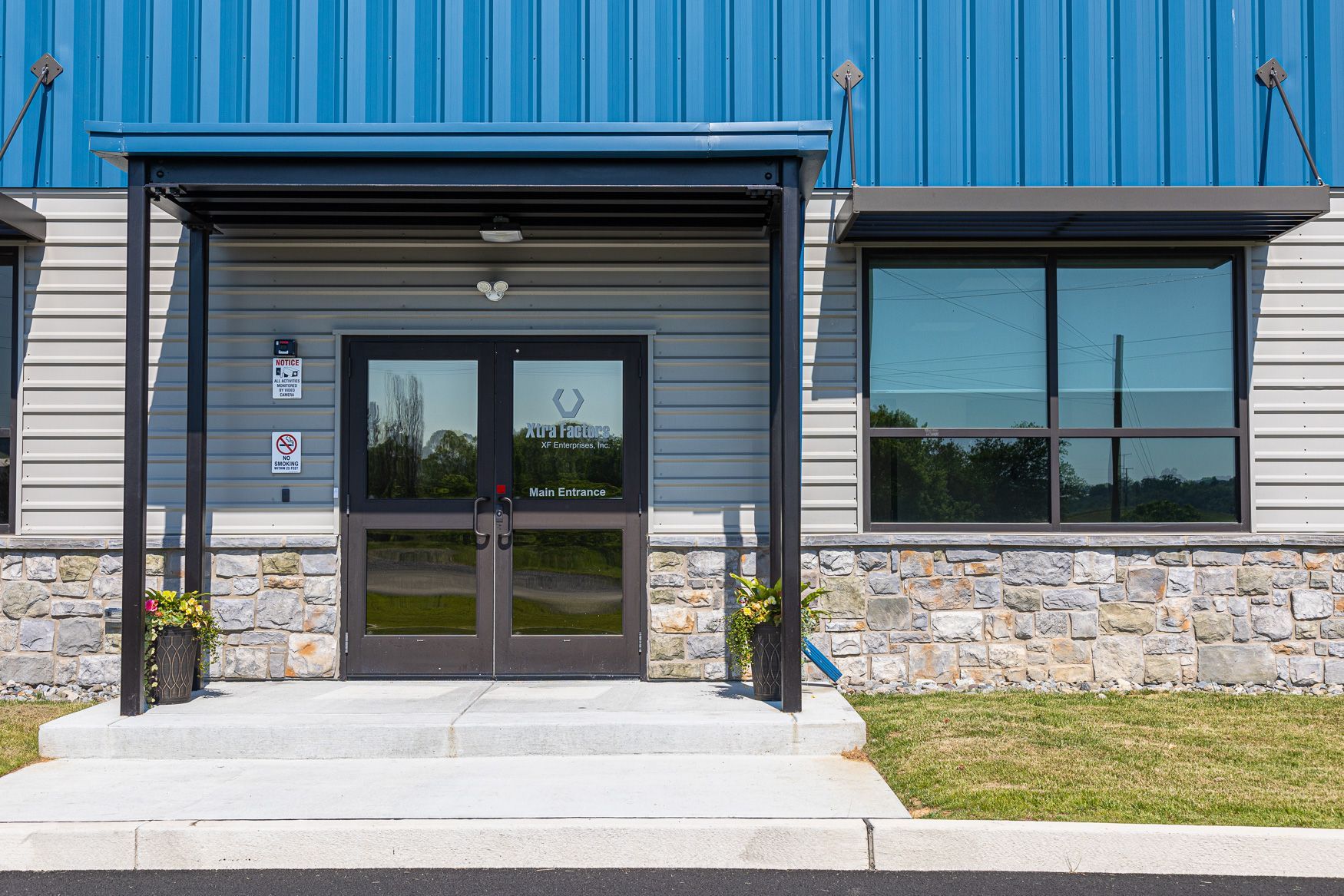 The entrance to the Xtra Factors East Earl, PA building with a blue roof and a stone wall.
