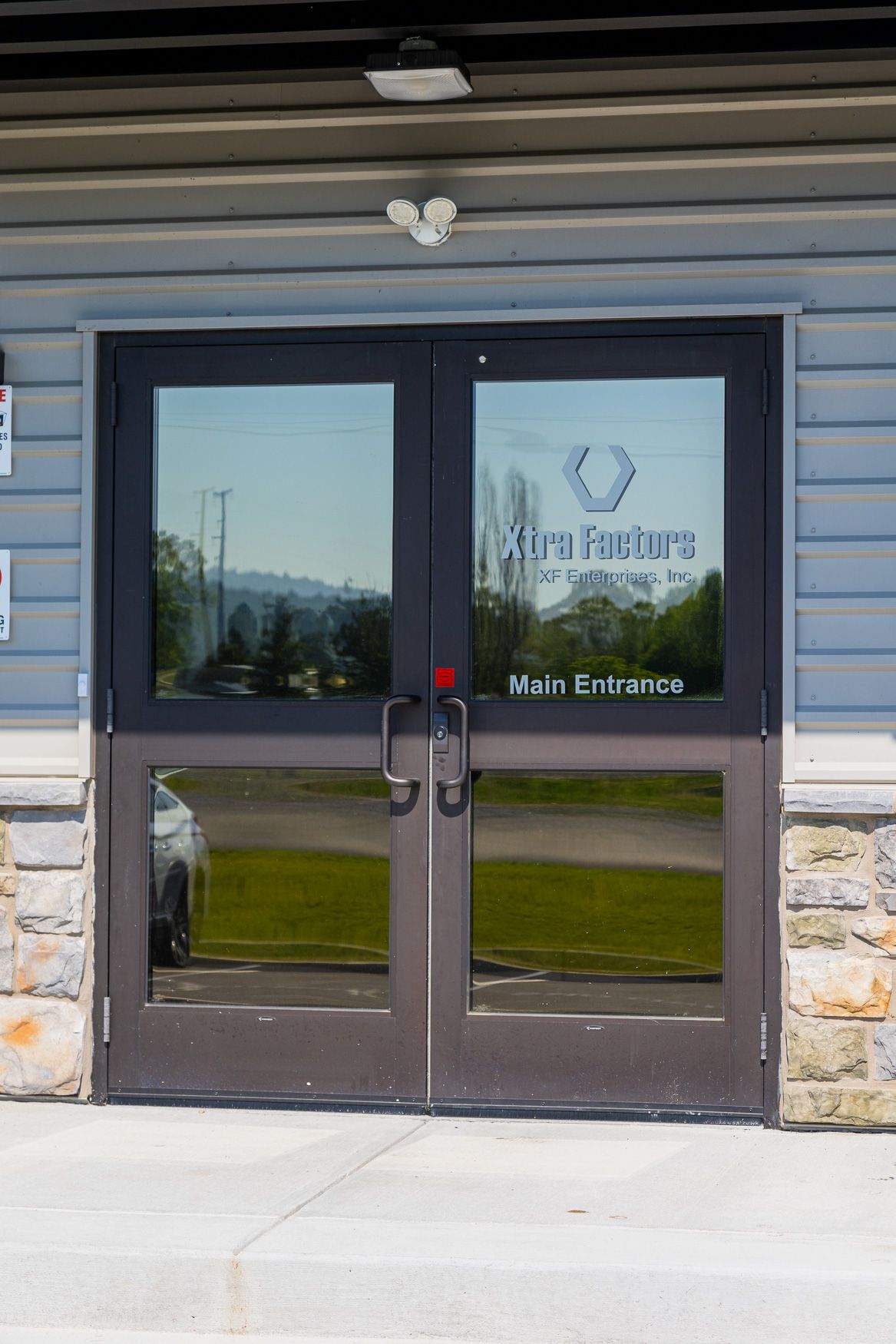 A pair of glass doors on the Xtra Factors East Earl, PA building with a car parked in front of them.