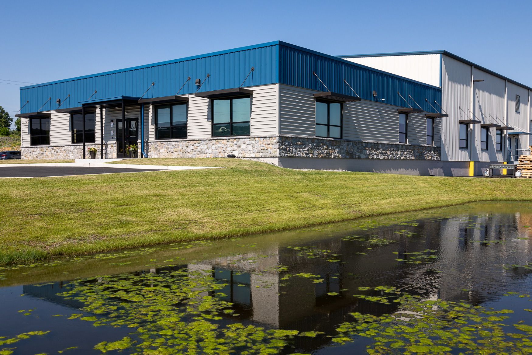 the Xtra Factors East Earl, PA building with a blue roof is sitting next to a pond.