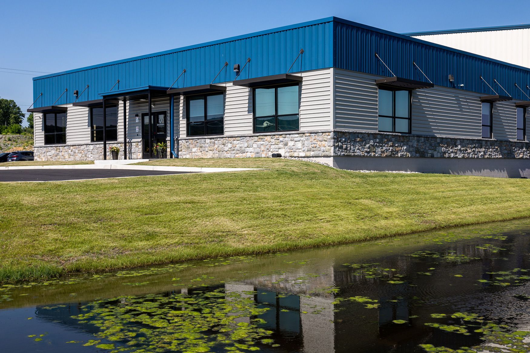 the Xtra Factors East Earl, PA building with a blue roof is sitting next to a body of water.