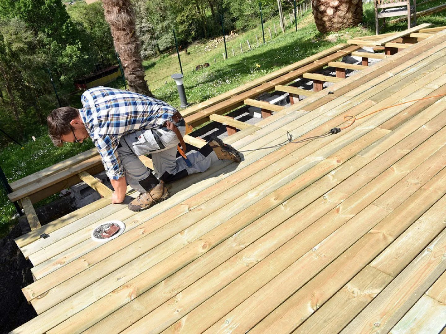 Worker installing wooden deck boards outdoors in a sunny yard