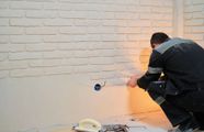 Technician in dark uniform working on a wall outlet, with sparks and orange light illuminating the scene
