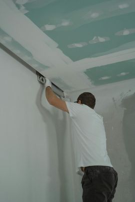 Person plastering a ceiling with a trowel in a room with unfinished drywall