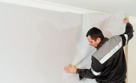 Man installing wallpaper on a wall, smoothing the paper into place.