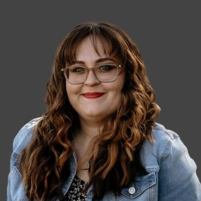 A woman wearing glasses and a denim jacket is smiling.