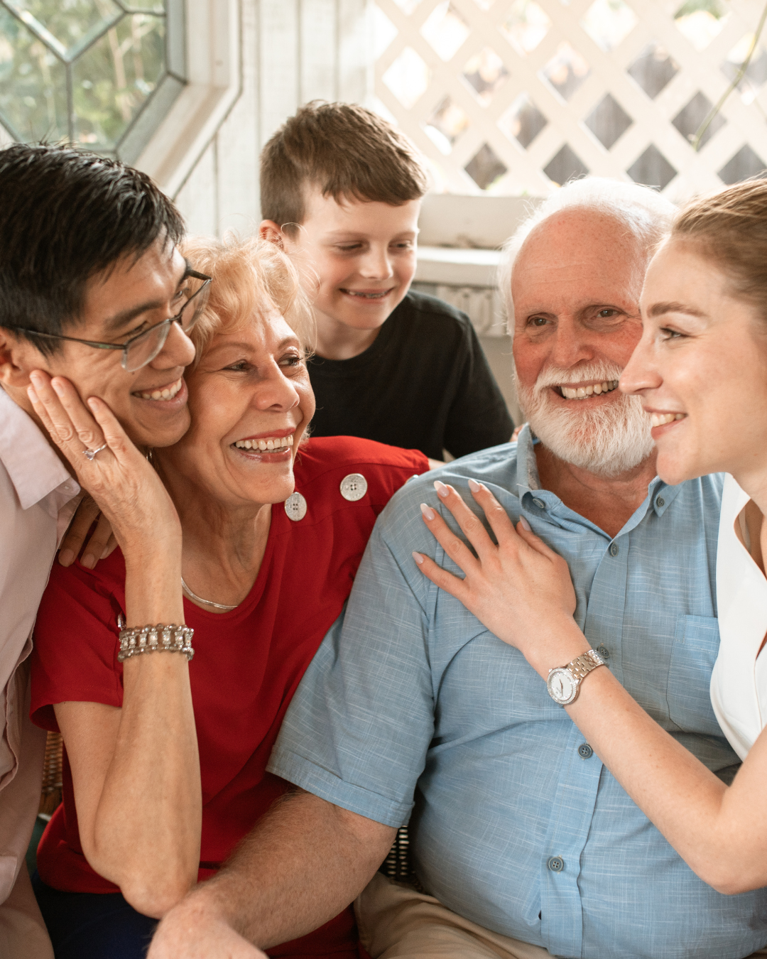 Family smiling and embracing indoors; grandparent, child, adult couple.