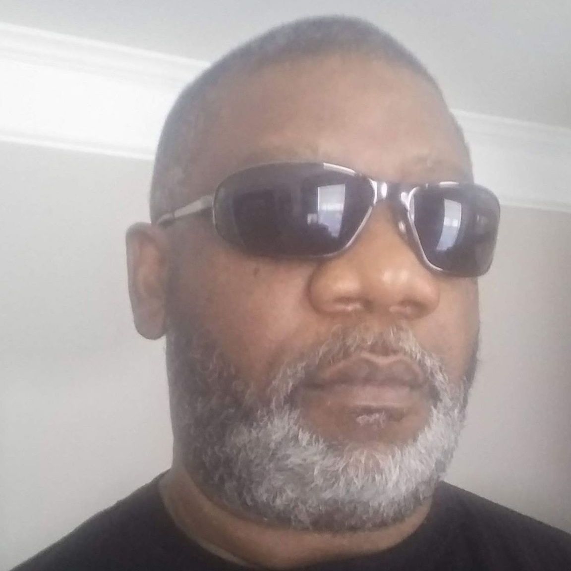 A man with a beard wearing sunglasses and a black shirt.
