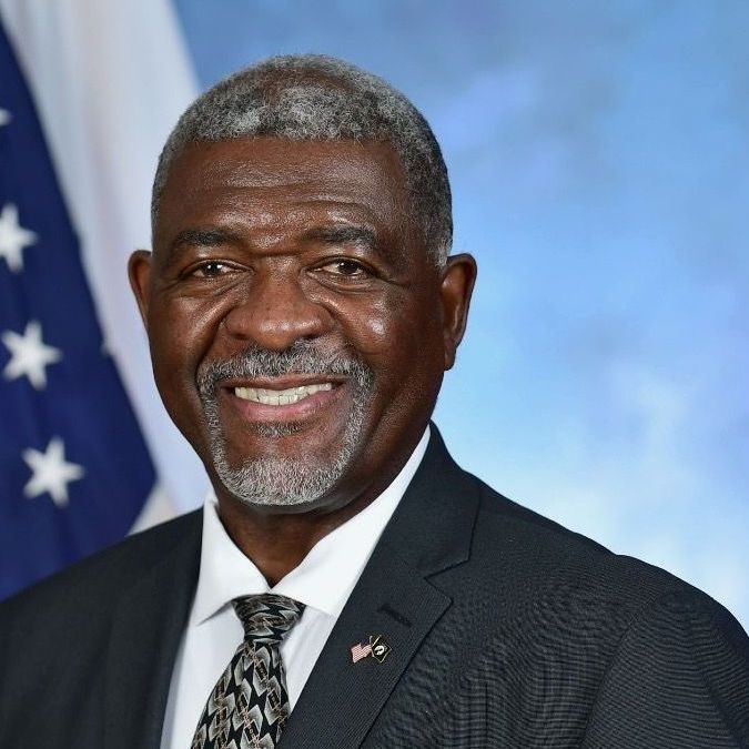 A man in a suit and tie is smiling in front of an american flag