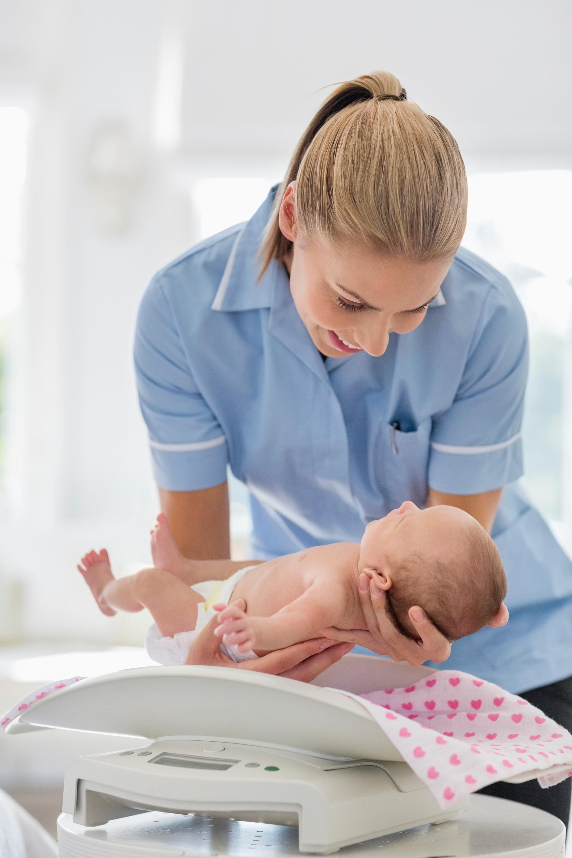 Nurse in blue uniform weighing a baby on a scale in a bright clinic