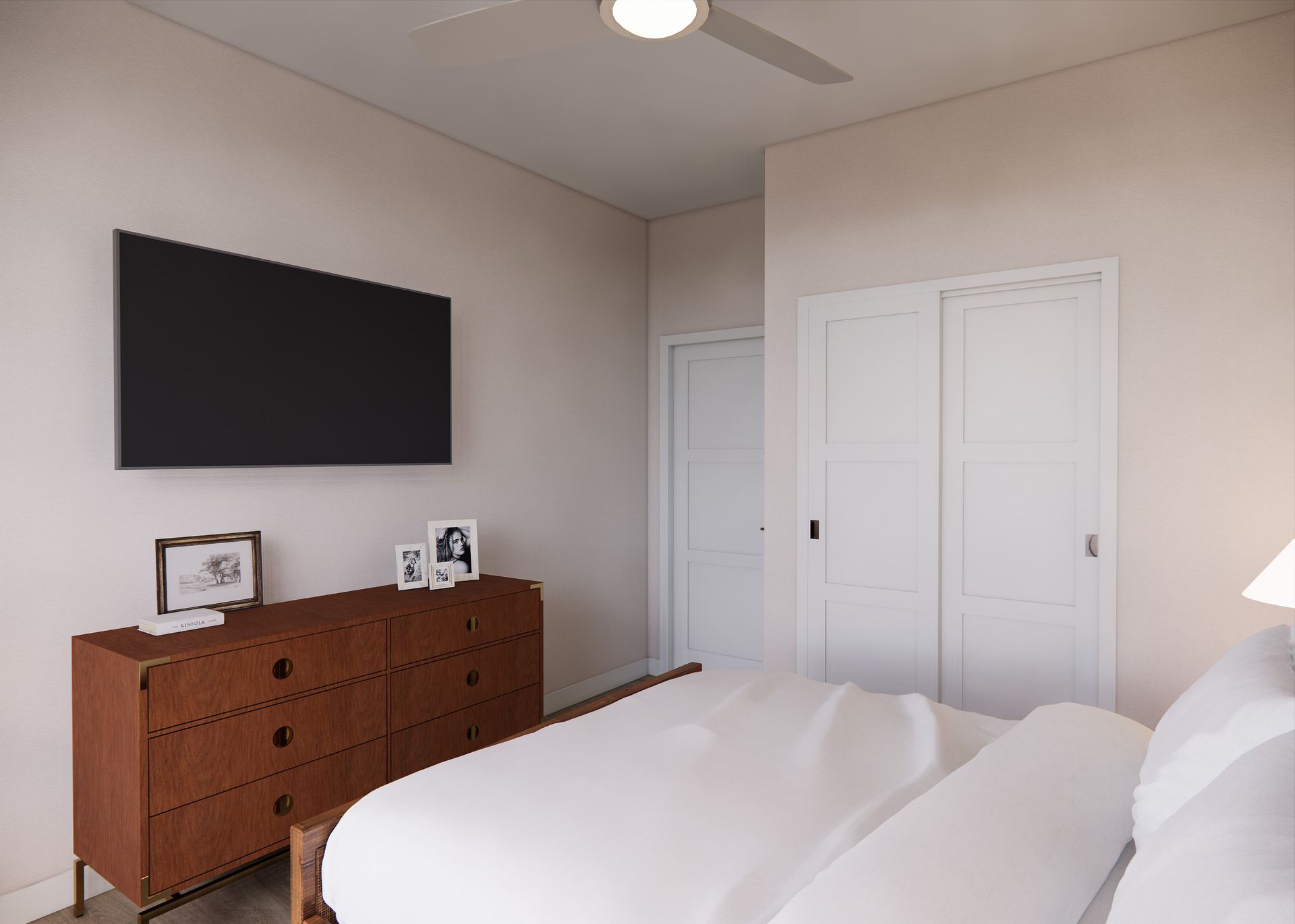 A bedroom with a bed in the foreground, a brown dresser with a mounted TV, a white closet, and a closed door.