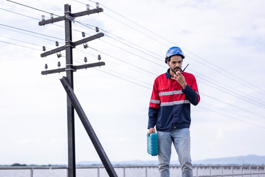 A man is standing next to a power line talking on a walkie talkie.