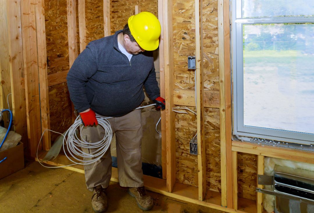 A man wearing a hard hat is holding a bunch of wires in a room.