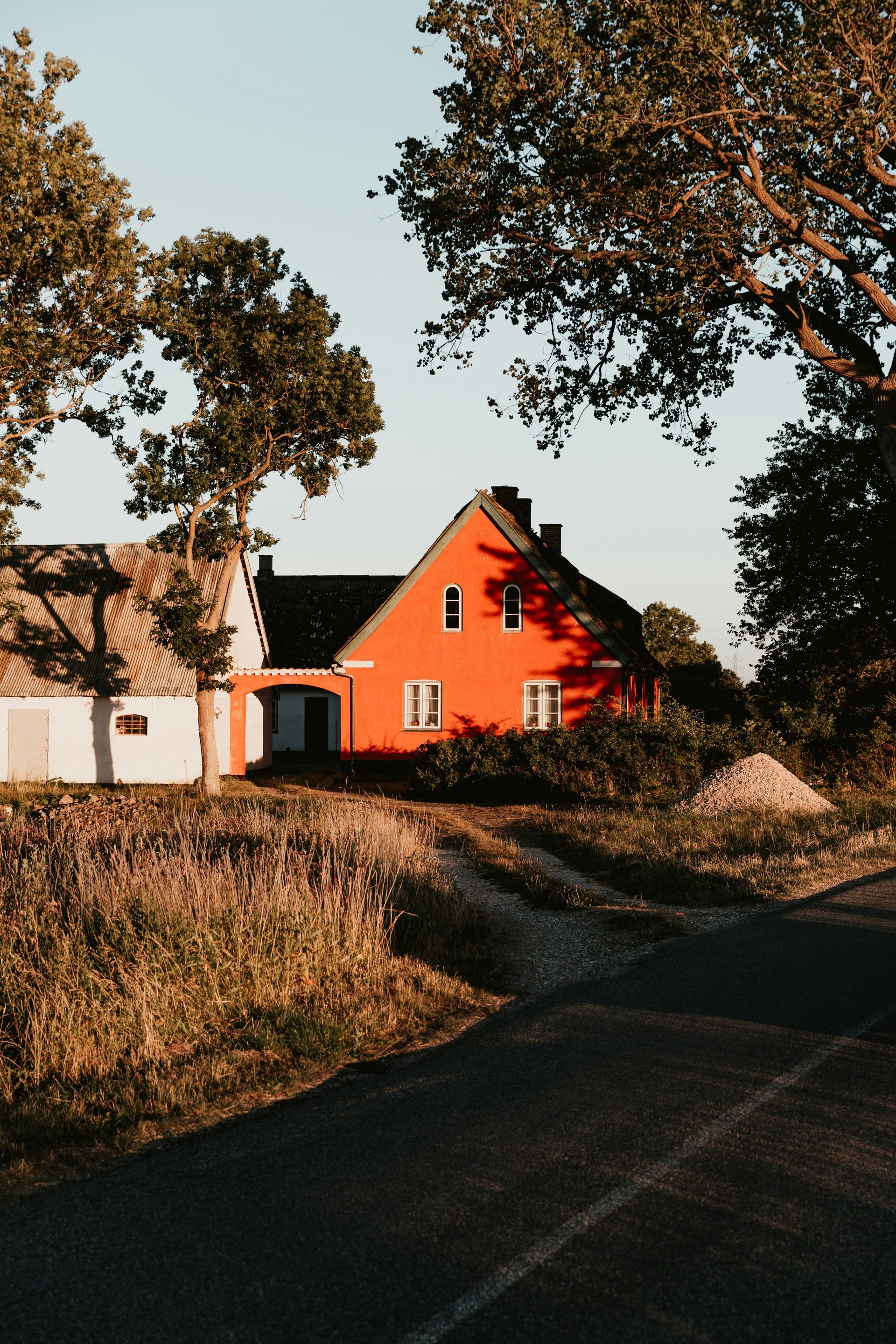 Een rood huis staat aan de kant van een zandweg.