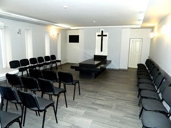 Šarvojimo salė su kėdžių eilėmis ir kryžiumi ant sienos