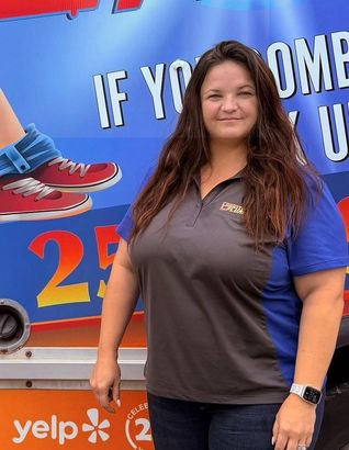 Woman in gray/blue shirt smiles in front of a service truck with text and shoe graphic.