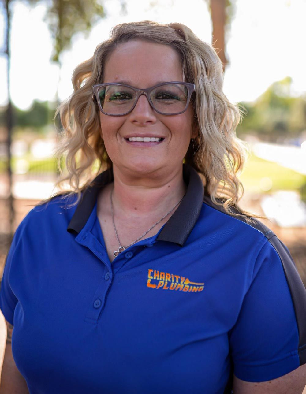 Woman with glasses smiles wearing blue polo shirt with logo.