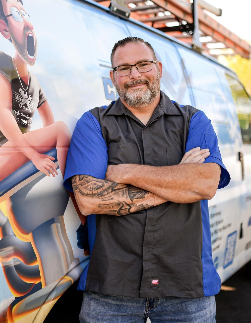 Man with crossed arms, standing in front of a company van, wearing a work shirt, and glasses.