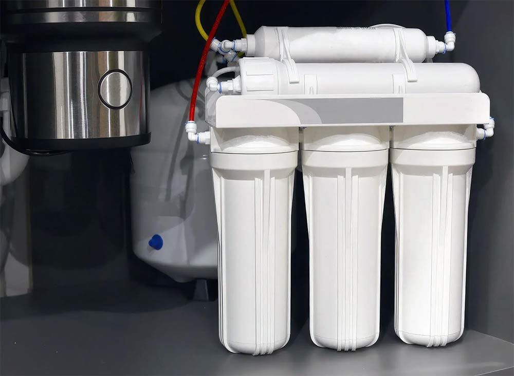 Water filtration system with multiple white filter housings and tubes in a cabinet.