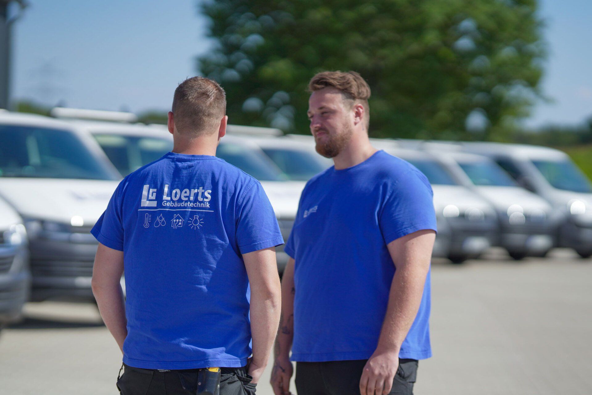 Zwei Loerts-Mitarbeiter stehen nebeneinander vor einer Reihe von Lieferwagen.