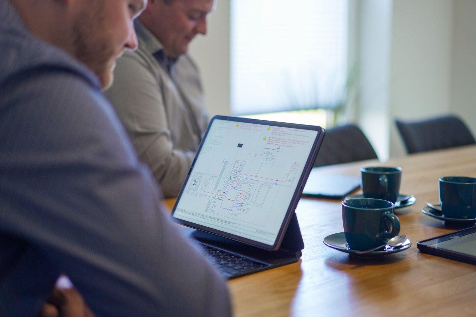 Zwei Männer sitzen an einem Tisch und schauen auf einen Laptop.