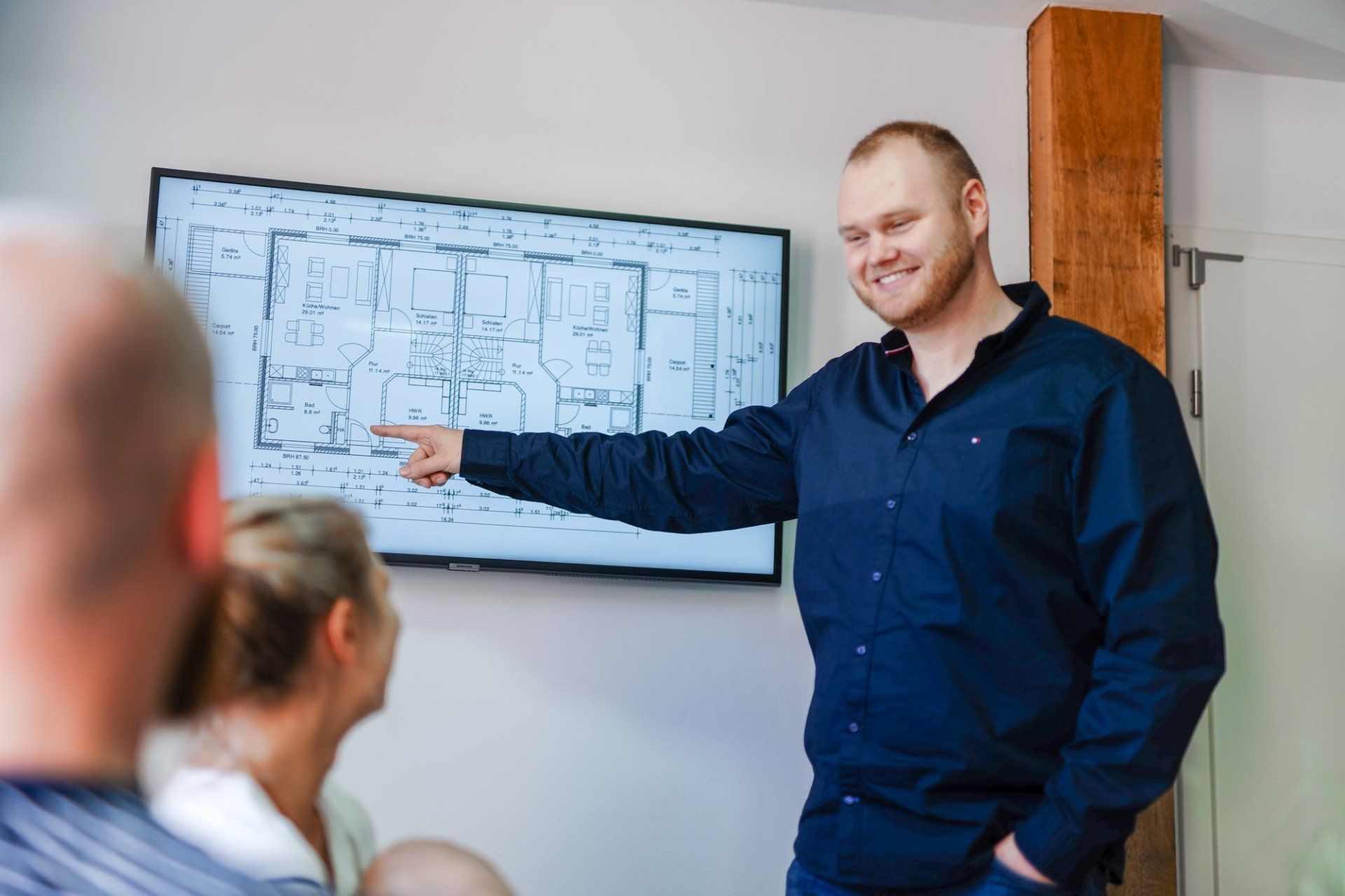 Ein Mann hält vor einer Gruppe von Leuten eine Präsentation und zeigt dabei auf einen Bildschirm.