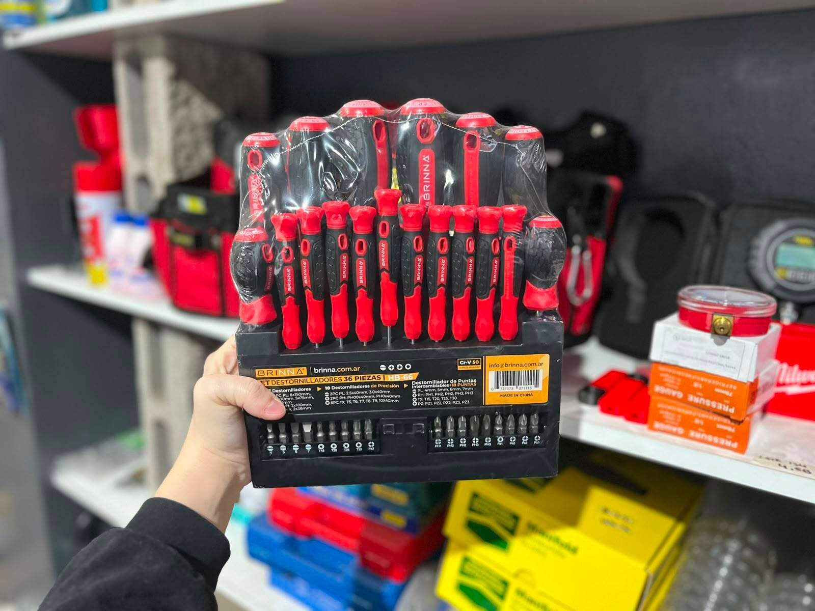 Una mano sostiene un juego de destornilladores rojos y negros frente a un estante de una tienda.
