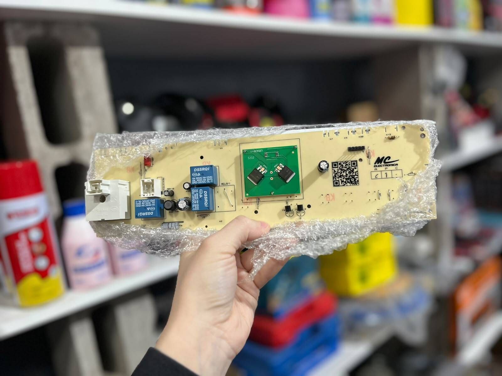 Mano sosteniendo una placa de circuito impreso montada sobre espuma con pequeños componentes electrónicos en un taller.