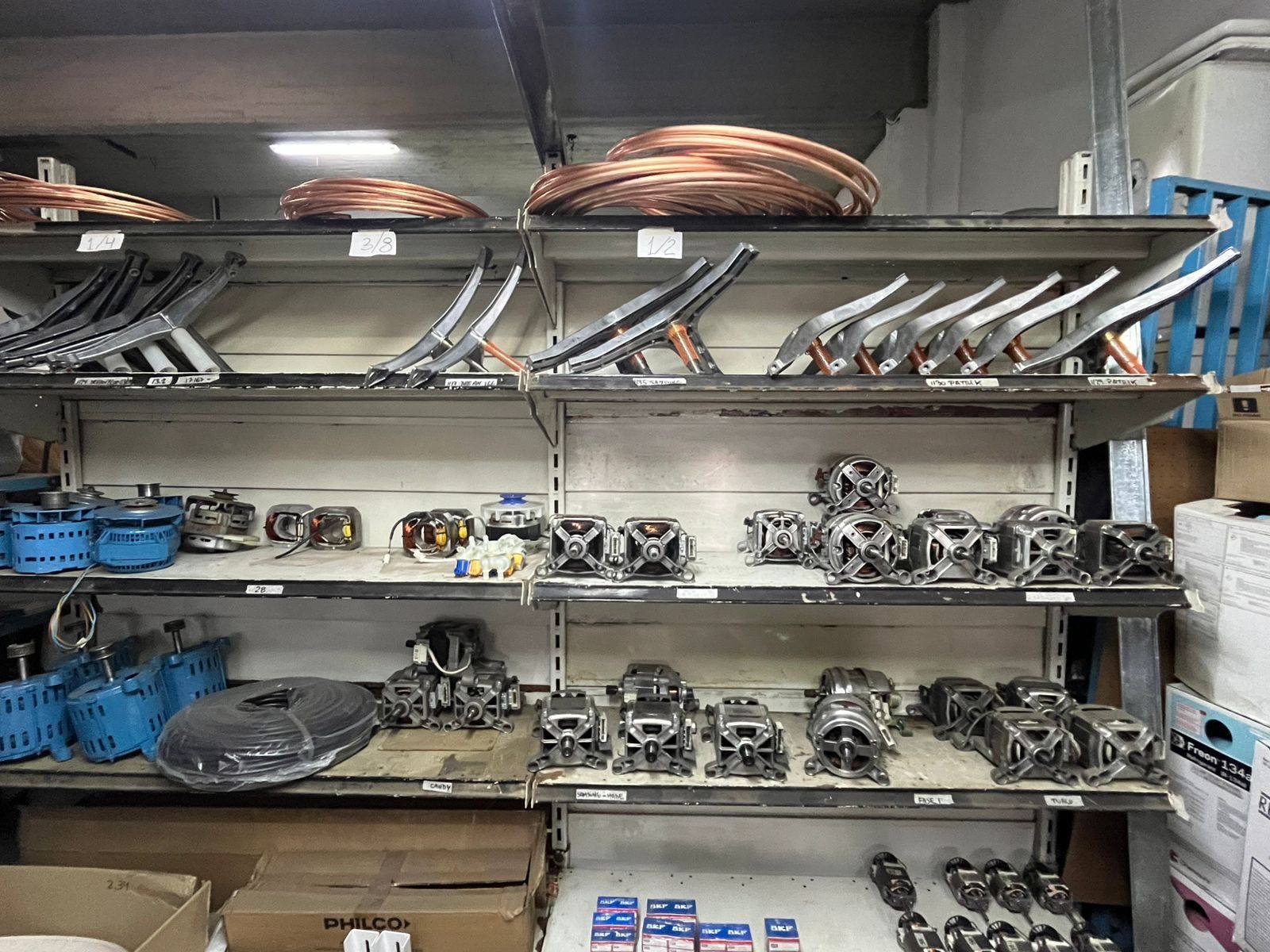 Estanterías en un taller repletas de piezas metálicas, herramientas y cables enrollados en contenedores de almacenamiento.
