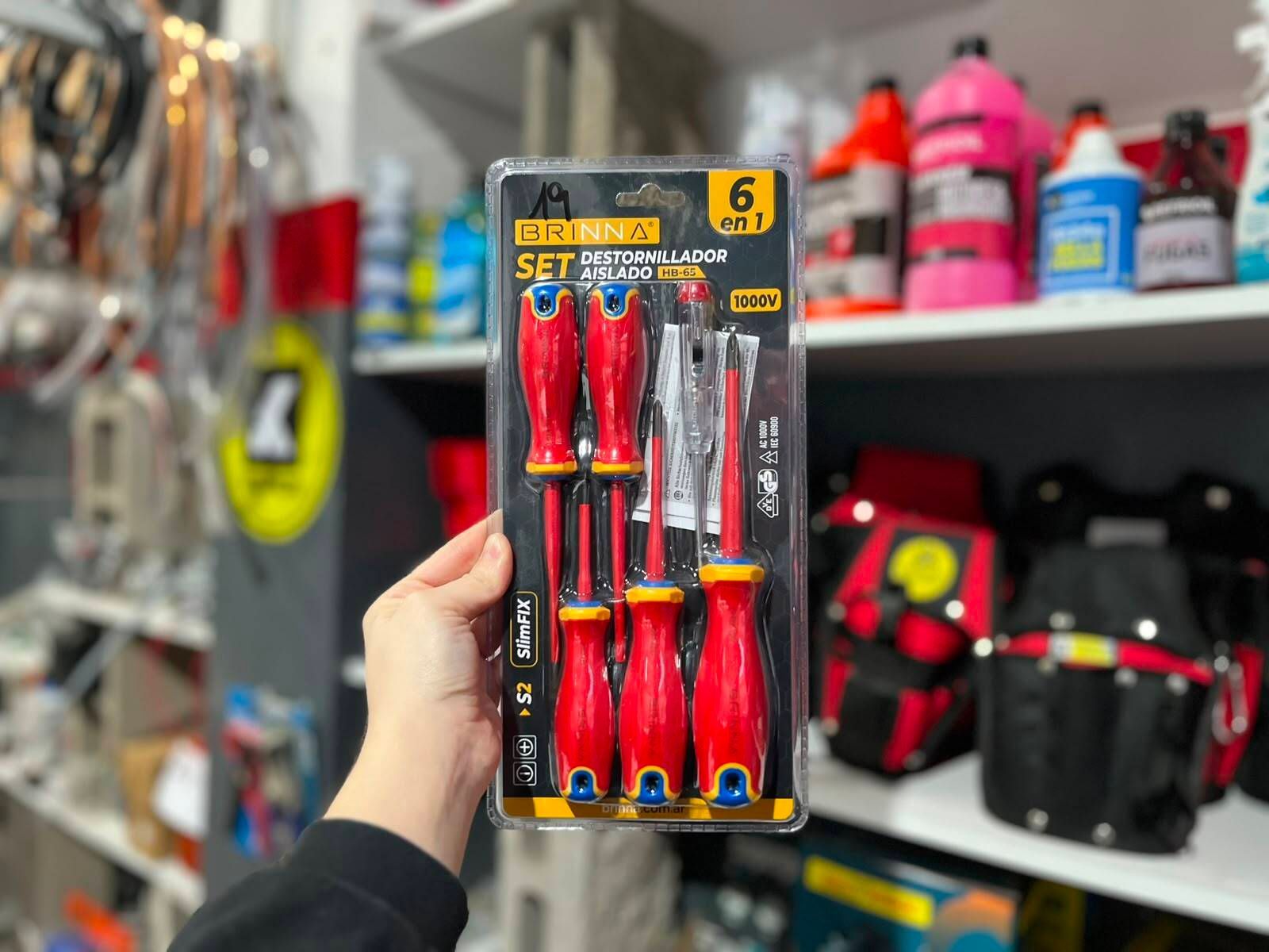 Una mano sostiene un paquete de destornilladores rojos en un pasillo de una ferretería.